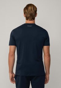 Donkerblauwe T-shirt met korte mouwen van katoen. Beschikt over een ronde hals en een logo gedrukt op de bovenrug. Gladde textuur, getailleerd ontwerp.