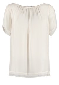 Blusa bianca leggera con vestibilità ampia, maniche corte e scollatura a barchetta. Tessuto morbido e trasparente con arricciature sulle spalle.