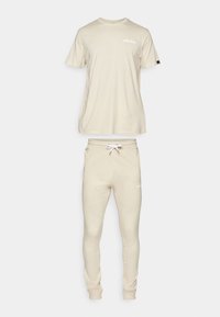Ensemble t-shirt à manches courtes en coton beige et jogging. Le t-shirt a un col rond ; le jogging présente une taille élastique et des poignets. Logo sur les deux articles.