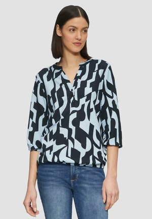 Blouse à motifs bleu et noir avec des manches trois quarts et un col en V, dotée de boutons et d'un tissu texturé.