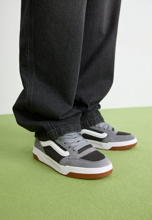 Gray suede and mesh sneakers with white accents, featuring a white midsole and rubber outsole. Worn with black tapered pants.