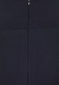 Tejido de color marino con un tejido texturizado que cuenta con una cremallera central. El detalle de las costuras encima de la cremallera añade un interés estructural a la forma de la prenda.