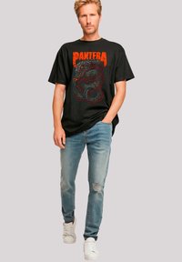 Schwarzes Baumwoll-T-Shirt mit einem roten Schlangengrafik und dem Text "Pantera". Kombiniert mit hellblauen, verwaschenen Jeans und weißen Turnschuhen.