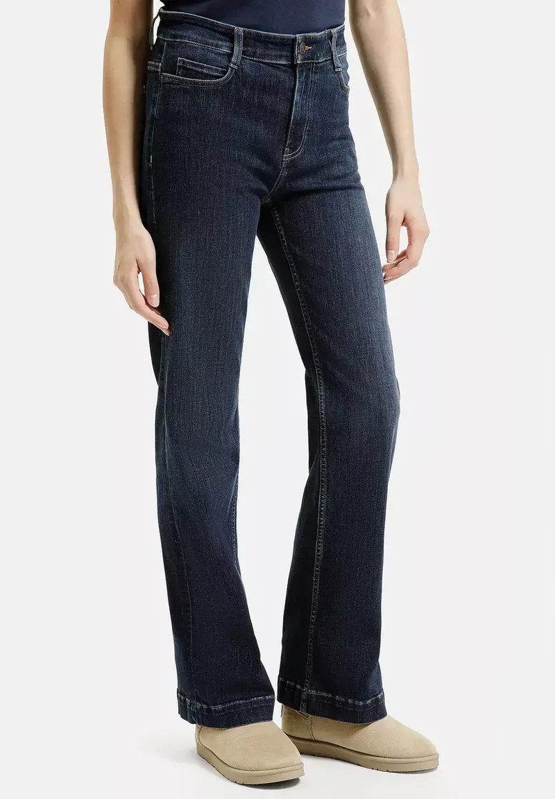 Ciemnoniebieskie dżinsy z denimu, o prostym kroju nogawki, pięciokomorowym stylu i subtelnym ściegowaniu. Połączone z beżowym obuwiem.