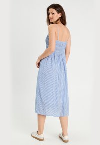 Robe midi rayée bleu clair avec des bretelles spaghetti, corsage smocké et jupe fluide. Associée à des baskets blanches, elle présente un look décontracté.
