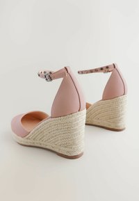 Pink faux leather wedge sandals with a woven jute platform and ankle strap, featuring a smooth texture and round toe design.