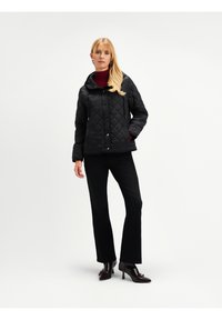 Czarna kurtka pikowana z kapturem, zapinana na napy, z bocznymi kieszeniami, w połączeniu z czarnymi spodniami dzwonami i ciemnymi trzewikami na obcasie.