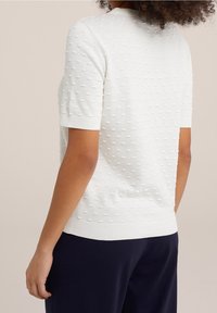 T-shirt à manches courtes, en tricot blanc, avec des détails en polka dots texturés, des poignets et un ourlet côtelés. Tissu doux avec une coupe décontractée.