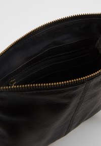 Interno di borsa in pelle nera con una texture liscia, con una tasca con cerniera e una rifinitura della cerniera in tono oro lungo il bordo.