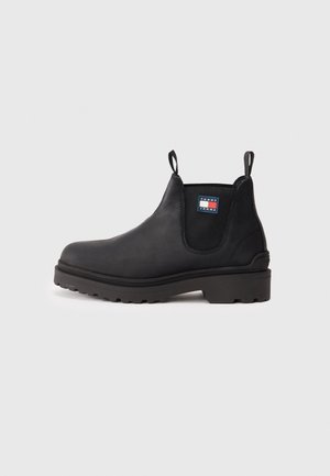 Botte Chelsea en cuir noir avec semelle épaisse à crampons, panneau latéral élastique, languettes de maintien et logo Tommy Jeans sur la cheville.