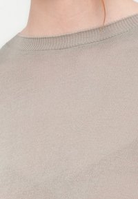 Licht beige gebreid top met een ronde halslijn. De stof heeft een gladde textuur en vertoont een subtiel ribbelpatroon langs de randen.