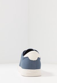 Modré plátěné tenisky s bílým pata a podešví, pohled zezadu, s brandingem "Hilfiger" na podešvi.