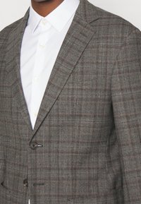 Grau kariertes Blazer mit taillierter Passform, ausgestattet mit einem Reverskragen, zwei Knöpfen und strukturiertem Stoff. Kombiniert mit einem weißen Hemd.