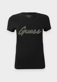 Must värviline puuvillane T-särk lühikeste varrukatega ja ümmarguse kaelusega, millel on ees suur, sädelev "Guess" logo metalllõngast.