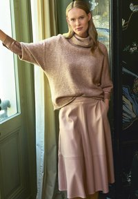 Lichtroze, oversized trui van zacht materiaal met een hoge nek, gecombineerd met een bijpassende geflanjeerde leren rok met nadendetails.