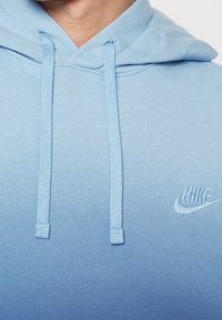 Sudadera azul de Nike con un diseño de degradado, que cuenta con un bolsillo tipo canguro, capucha con cordón y logo bordado en el pecho.