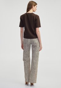Bruine top met korte mouwen en een ronde hals, gecombineerd met beige gestippelde wijde broekspijpen met een subtiel gemêleerd patroon en zijzakken.
