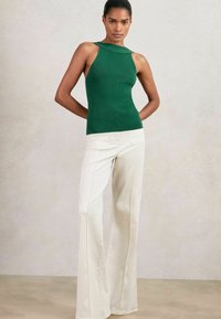 Grünes, geripptes Tanktop mit einzigartigem Schulterdesign, kombiniert mit hochtaillierten weißen ausgestellten Hosen, die über eine dezente Nahtdetails verfügen.