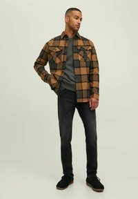 Brown and black plaid shirt jacket with two chest pockets, worn over a gray shirt, paired with black slim-fit jeans and black shoes.