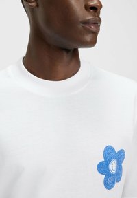 White sweatshirt featuring a blue flower design on the left chest, with a smiley face in the center. Soft texture, ribbed neckline.