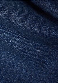 Ingrandimento di un tessuto denim blu scuro che mostra la texture dettagliata e il motivo di trama diagonale.