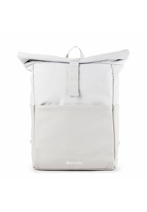 Mochila de color gris claro con cierre enrollable, bolsillo frontal y cierre de lazo de tela, con el logo "Bench." en el centro inferior.