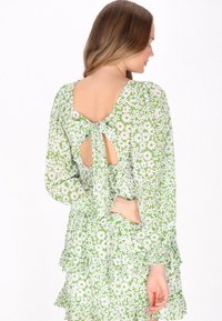 Rochie florală verde cu talie smock, mâneci volănaș și spate deschis cu detaliu de fundă. Material ușor cu o textură moale.