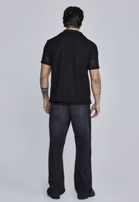 Camisa polo negra de canalé con mangas cortas, combinada con pantalones de mezclilla oscuros con costuras sutiles y dos bolsillos traseros.
