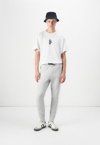 White cotton t-shirt with graphic print, gray sweatpants with drawstring waist, and black bucket hat. White and gray athletic shoes.
