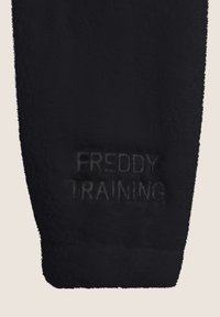 Giaccone in pile nero con una morbida texture, caratterizzato da un dettaglio testuale in rilievo "FREDDY TRAINING" in una tonalità più scura e sobria.