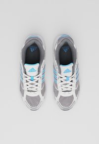 Adidas sportskor med en grå meshovandel, vita detaljer, blå ränder och en vadderad krage. Platta skosnören och detaljerad texturerad sula syns.