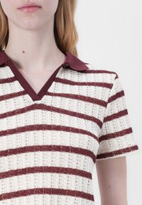 Strick-Polohemd mit senkrechten burgunderfarbenen und cremefarbenen Streifen, V-Ausschnitt und kurzen Ärmeln. Der Stoff hat ein strukturiertes, offenes Gewebe.