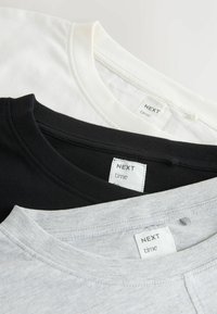 Trzy koszulki w kolorze czarnym, białym i szarym, z okrągłymi dekoltami i metkami marki. Tkanina wydaje się miękka, z typowymi szwami.
