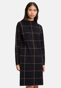 Svart långärmad klänning med figursydd passform, prydd med ett rutmönster i orange. Tillverkad av ett mjukt tyg med hög hals.