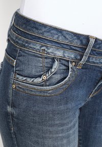Jeans de denim en un lavado azul medio, con una cinturilla de altura media, cinco bolsillos y detalles de costura en contraste.