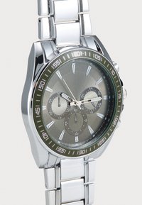 Silver metal watch with a grey dial, three sub-dials, and white hour markers. The bezel features a contrasting dark green accent.