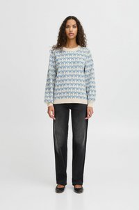 Suéter de punto con patrón de lazo azul sobre un fondo claro; puños y dobladillo acanalados. Combinado con jeans rectos negros y bailarinas negras.