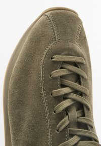 Olivgrüner Wildledersneaker mit runder Zehenpartie, flachen Schnürsenkeln und tonalem Stich. Strukturierte Oberfläche und eine flexible Gummisohle.