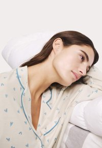 Maglietta da pigiama beige chiaro con piccoli motivi a forma di cuore blu, caratterizzata da un colletto a piping e una tasca sul petto. Tessuto morbido, vestibilità rilassata.