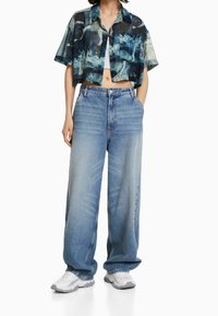 Kortärmad, urklippt skjorta med en blå abstrakt mönstring; kombinerad med vida ljusblå denimjeans och vita sneakers.