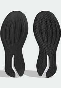 Semelles de chaussures en caoutchouc noir avec des motifs texturés, présentant des rainures pour l'adhérence et un accent blanc sur le côté.