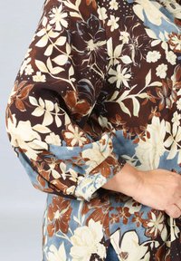 Brown floral-patterned shirt with cream and blue accents. Features three-quarter sleeves and a buttoned cuff. Smooth fabric texture.