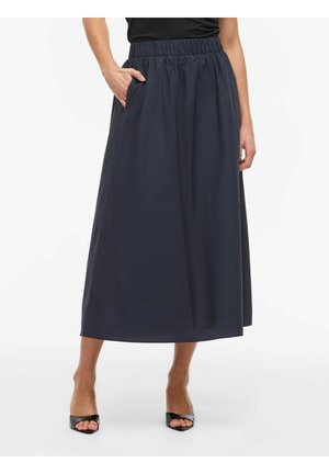 Frau trägt einen marineblauen Midirock mit elastischem Bund, seitlichen Taschen und schwarzen offenen High Heels, steht vor einem weißen Hintergrund.