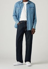 Jeansskjorta i ljusblått, knäppning framtill med två bröstfickor. Bärs över en vit t-shirt med rund halsringning och matchas med mörka jeans och vita sneakers.