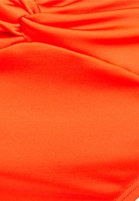 Tecido elástico laranja brilhante com uma textura suave, apresentando detalhes drapeados e um brilho subtil, adequado para trajes de banho ou vestuário desportivo.