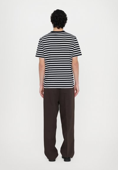 Camiseta de rayas blancas y negras con cuello redondo, combinada con pantalones sueltos de color marrón oscuro. El tejido parece suave con una silueta ajustada.
