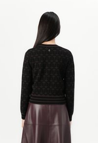 Pull en maille noir avec un motif géométrique, poignets et ourlet côtelés. Associé à une jupe en cuir bordeaux, texture lisse.