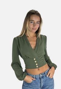 Grüne Wickelbluse mit langen, puffigen Ärmeln und Holzknöpfen vorne. Verfügt über einen tiefen V-Ausschnitt und ein kurzes Design.