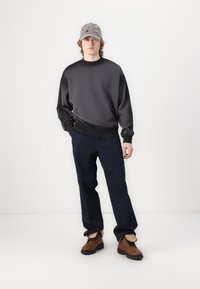 Gray sweatshirt with a round neck, navy trousers, and brown boots. The cap is gray with colorful embellishments. Simple, casual design.