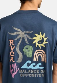 Camiseta de cuello redondo de color azul marino con estampados en varios colores: palmera, sol, cara, arcoíris, olas y el texto "BALANCE DE OPUESTOS."